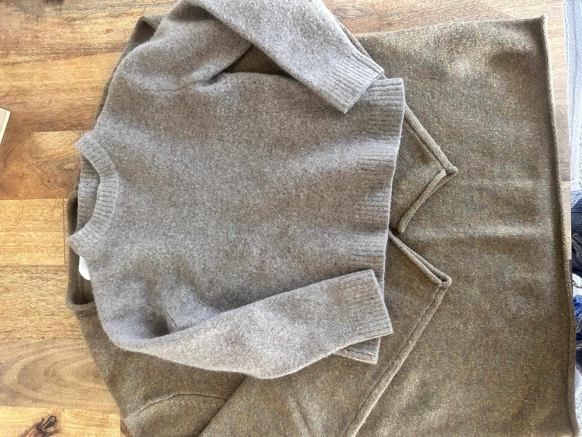 A wool sweater shrunk in the dryer, laid on top of a sweater that used to be the same size